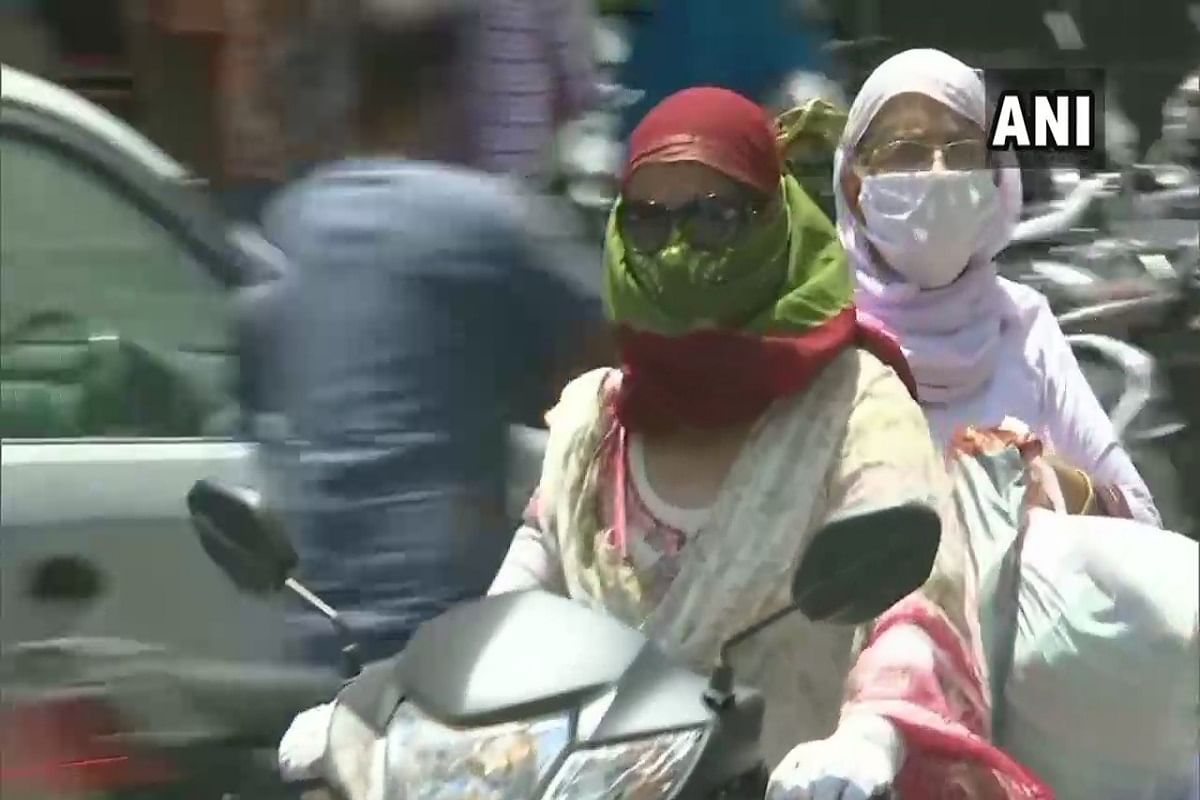 गर्मी से बचने के लिए खुद को ढककर वाहन चलाती महिला