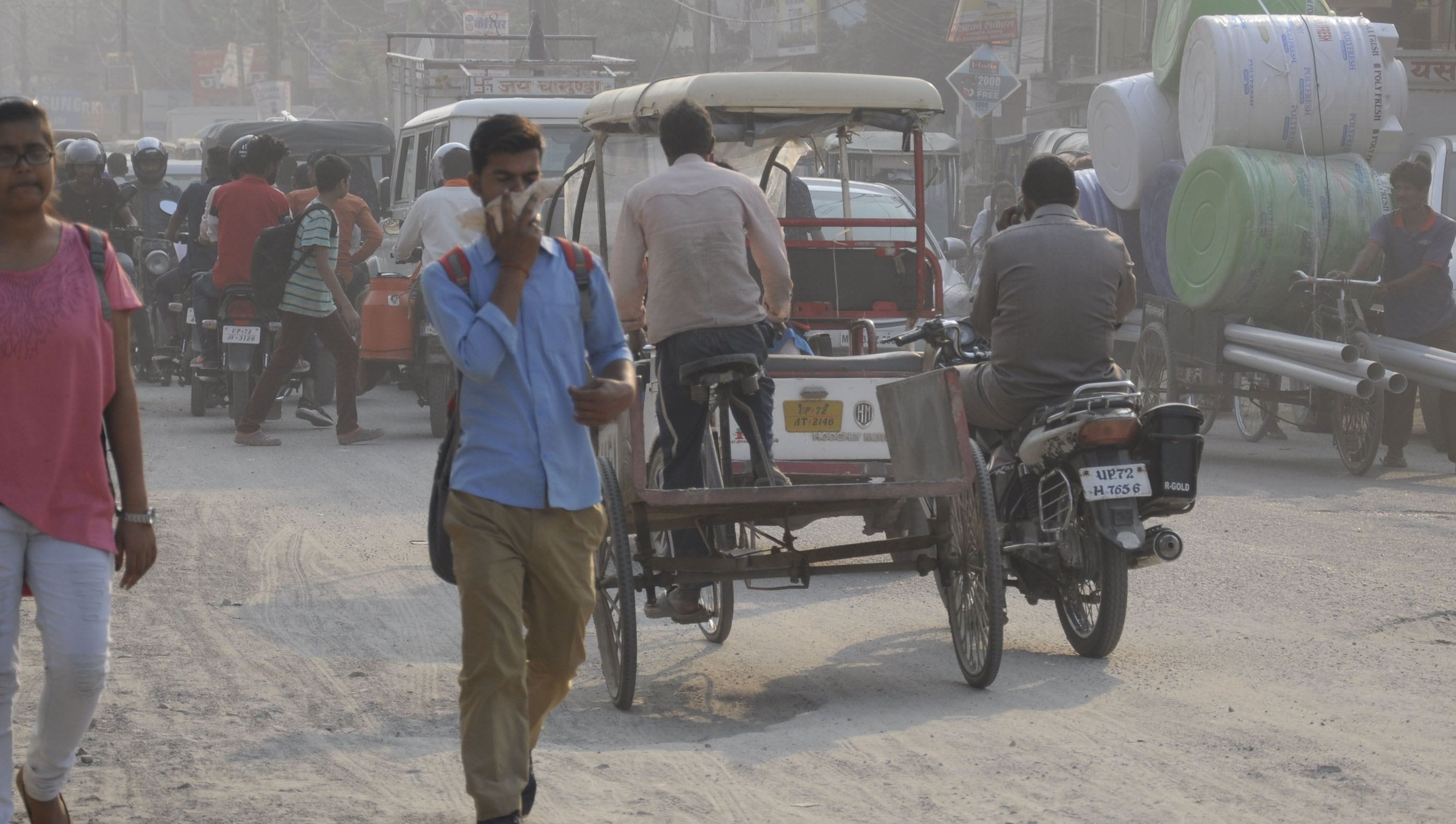 स्टेशन के समीप सड़क पर उड़ रही धूल से बचने को मुंह ढंके छात्र।