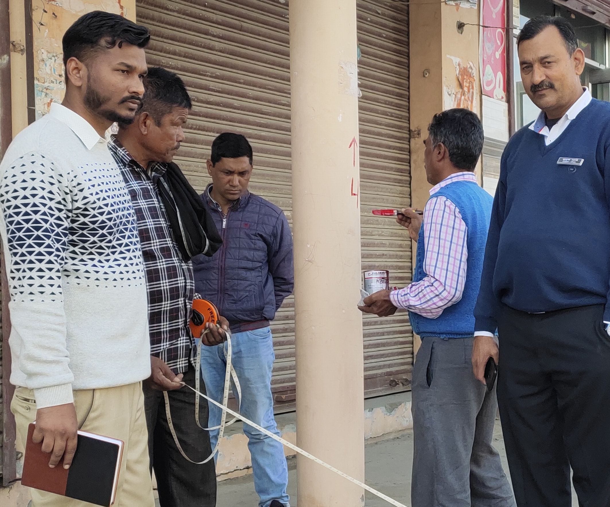 सितारगंज मीना बाजार में नपत कर लाल निशान लगाते लोनिवि कर्मी।