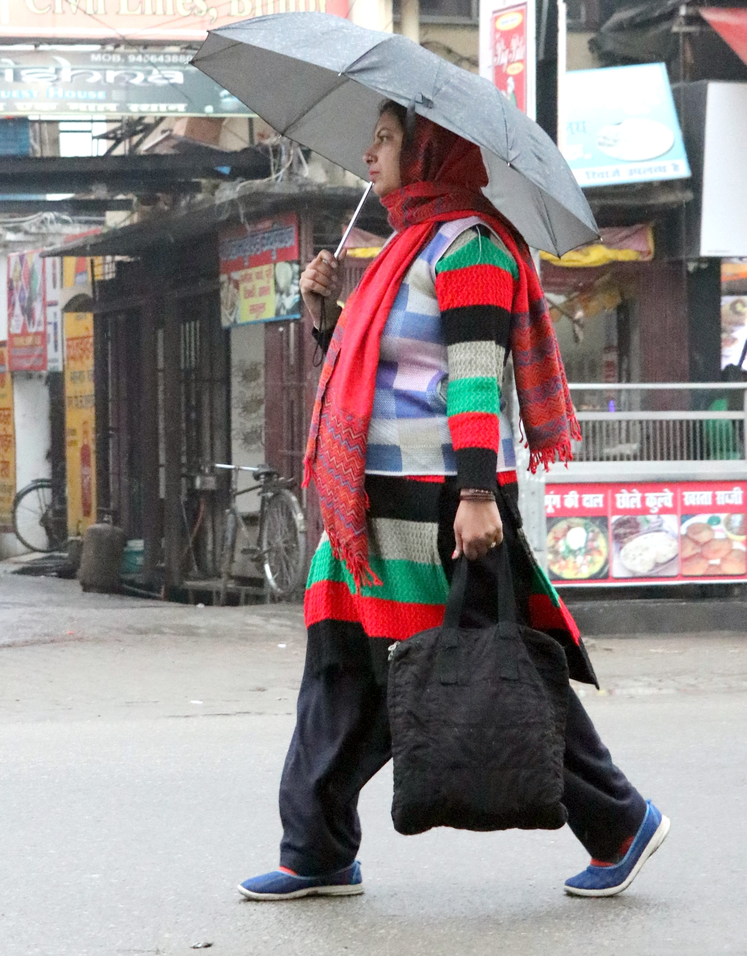 बिजनौर में बारिश में छाता लगाकर जाती महिला।
