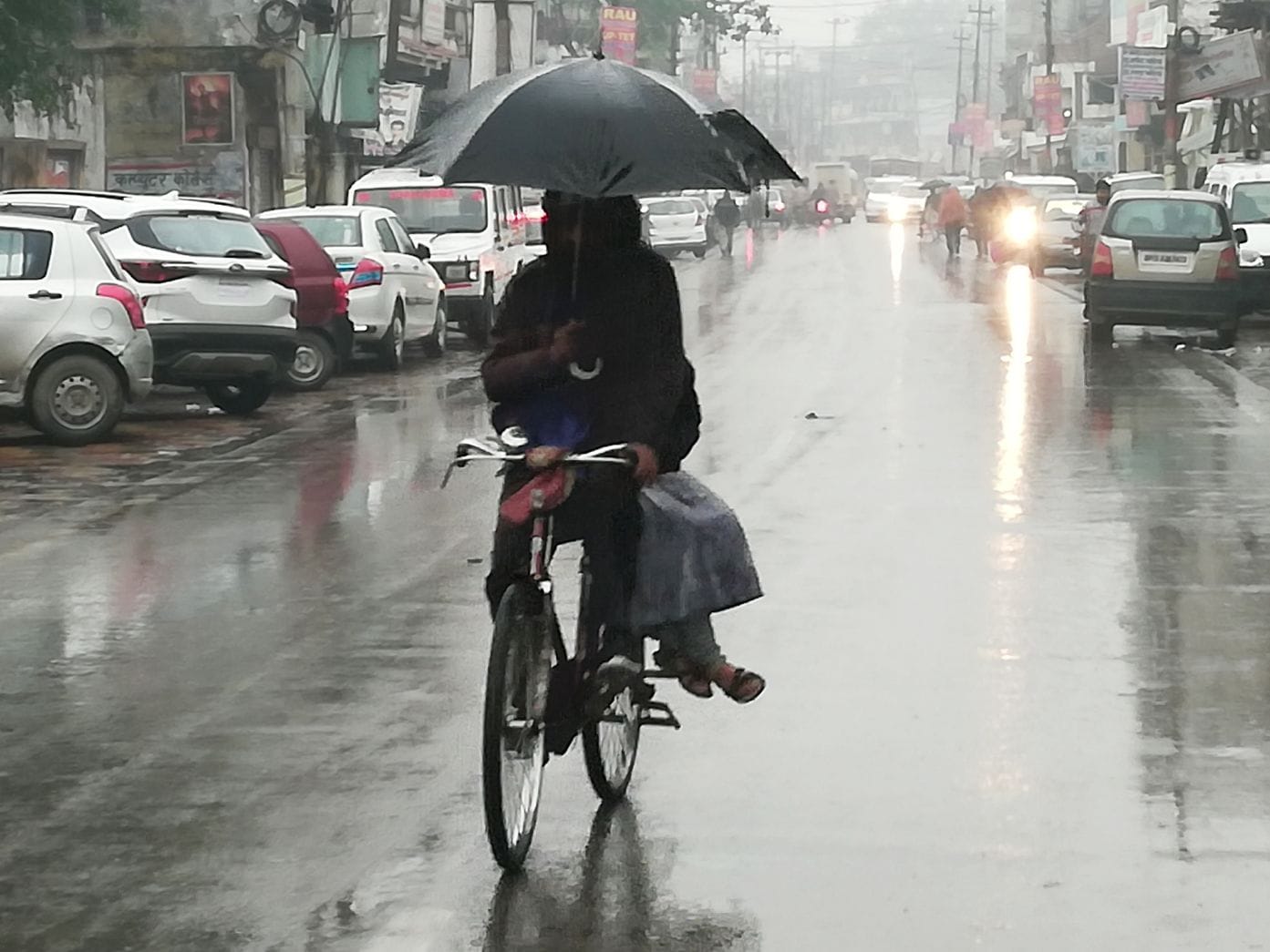 बारिश के कारण सूना पड़ा मुख्य मार्ग, साइ्किल पर छाता लगाकर जाता व्यक्ति।