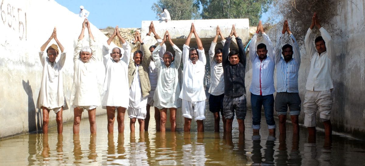  रेलवे अंडरपास में भरे पानी में खड़े होकर योग करते ग्रामीण।