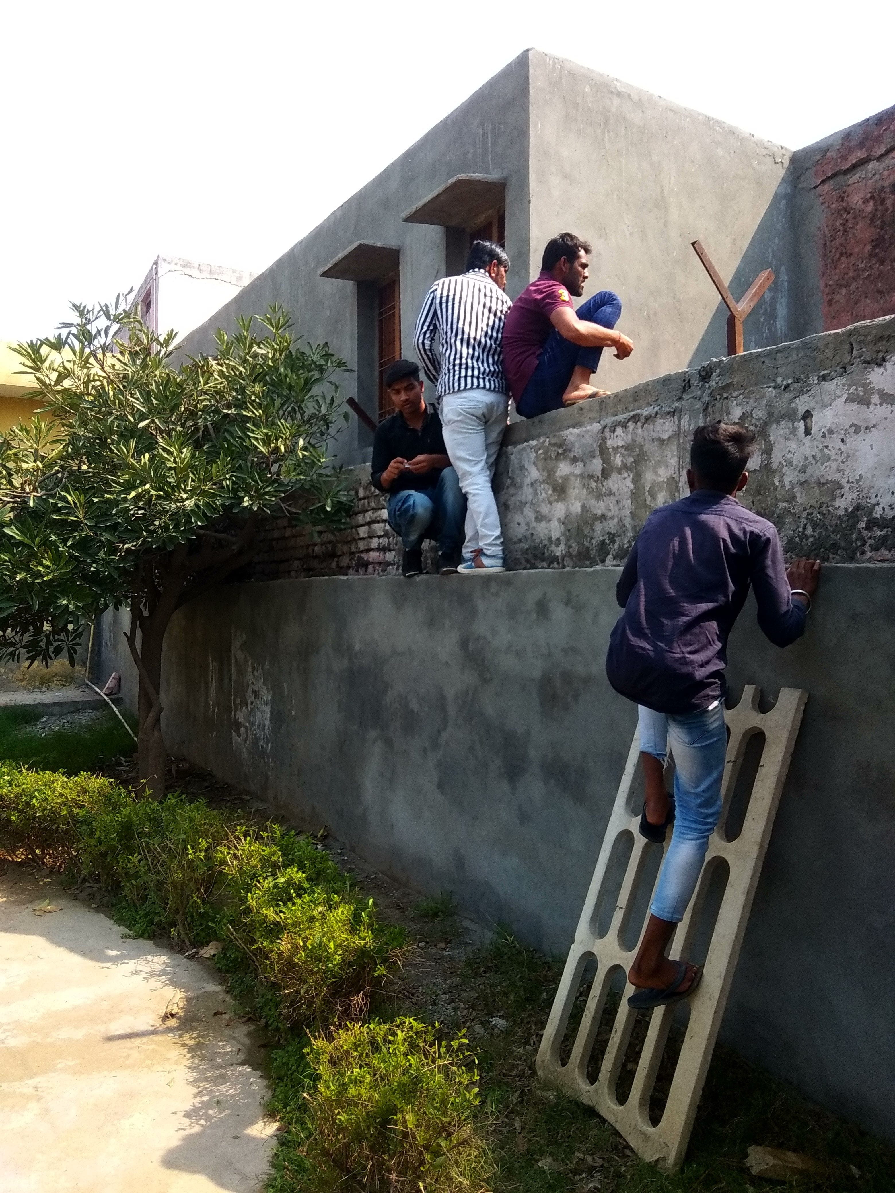 नकल डालने के लिए परीक्षा केंद्र की दीवार पर चढ़े युवक।