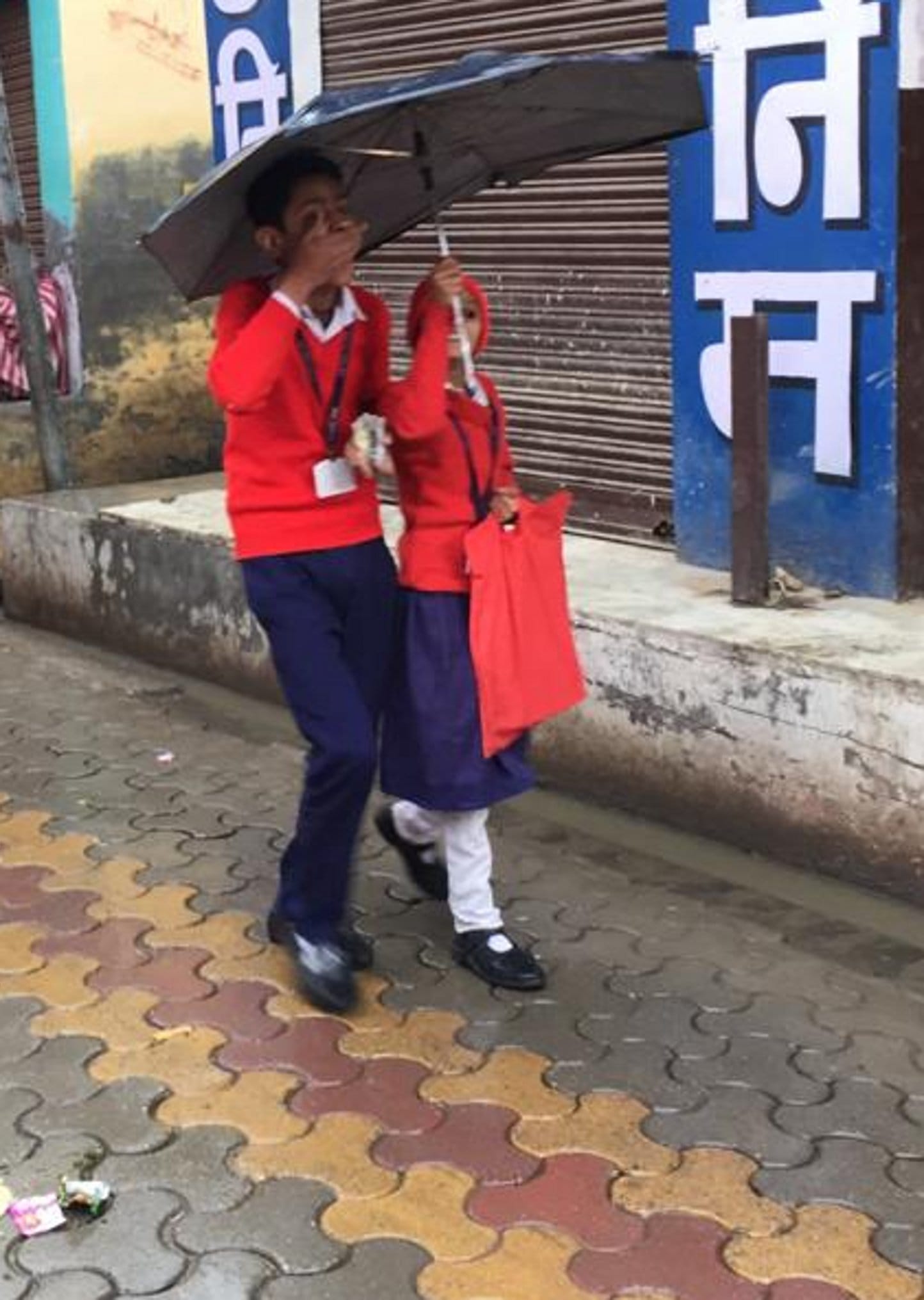 ऊन बरसात में छाता लगा कर जाते स्कूली बच्चे