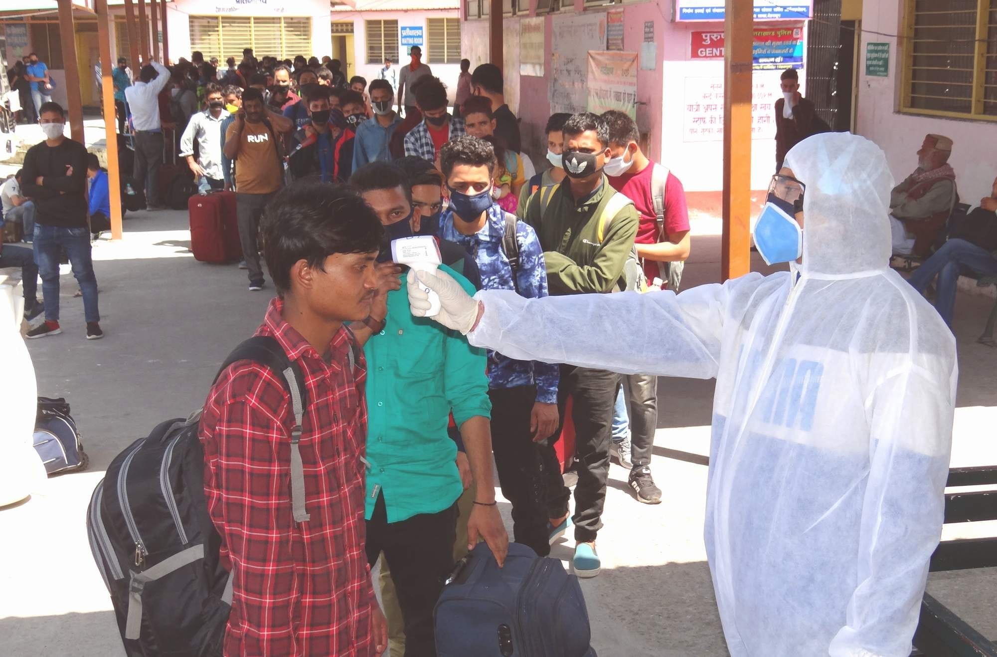 बस अड्डे पर पहाड़ी रूटों पर जाने वालों की थर्मल स्क्रीनिंग करता स्वास्थ्य कर्मी।