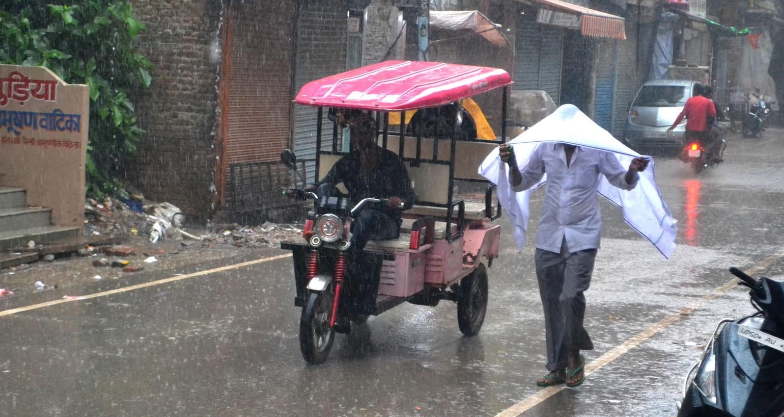 सुबह हुई जोरदार बारिश में भींगते हुए जाते लोग।