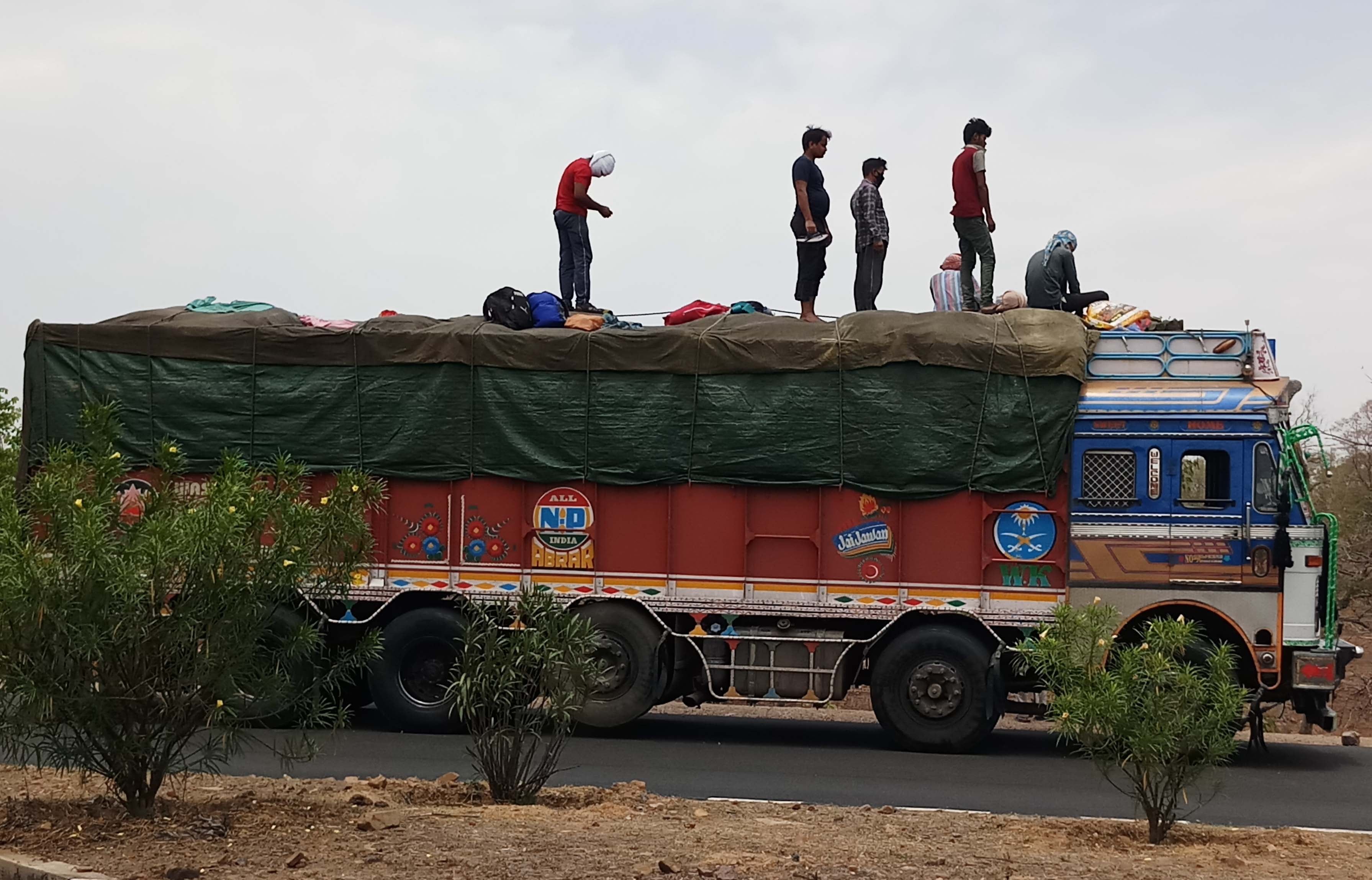 ट्रक पर बैठकर सफर करते लोग