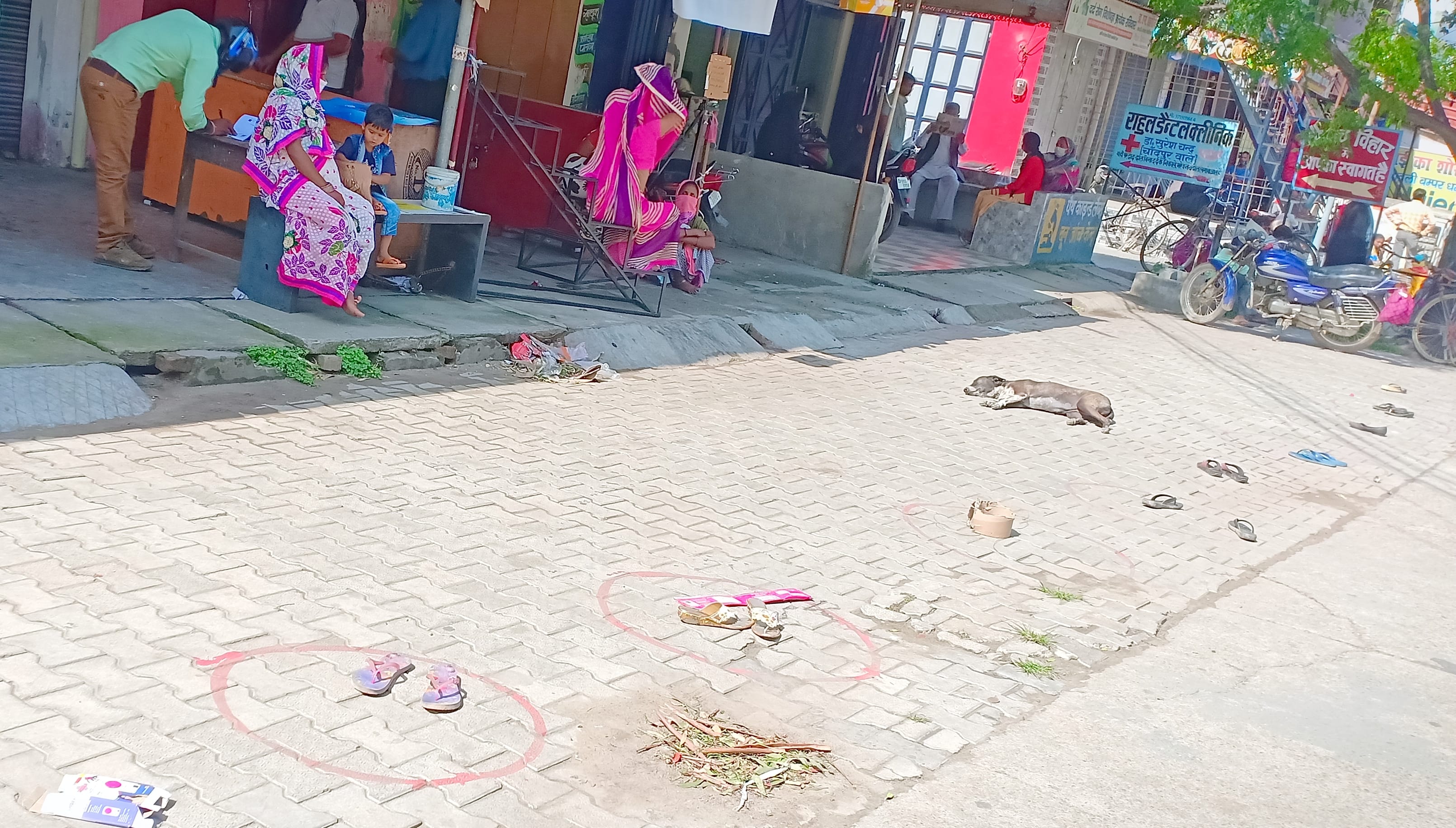 नगीना में बैंक ऑफ इंडिया शाखा के बाहर बने गोल घेरे मैं चप्पल ईट रखकर छाया में बैठी महिलाएं।