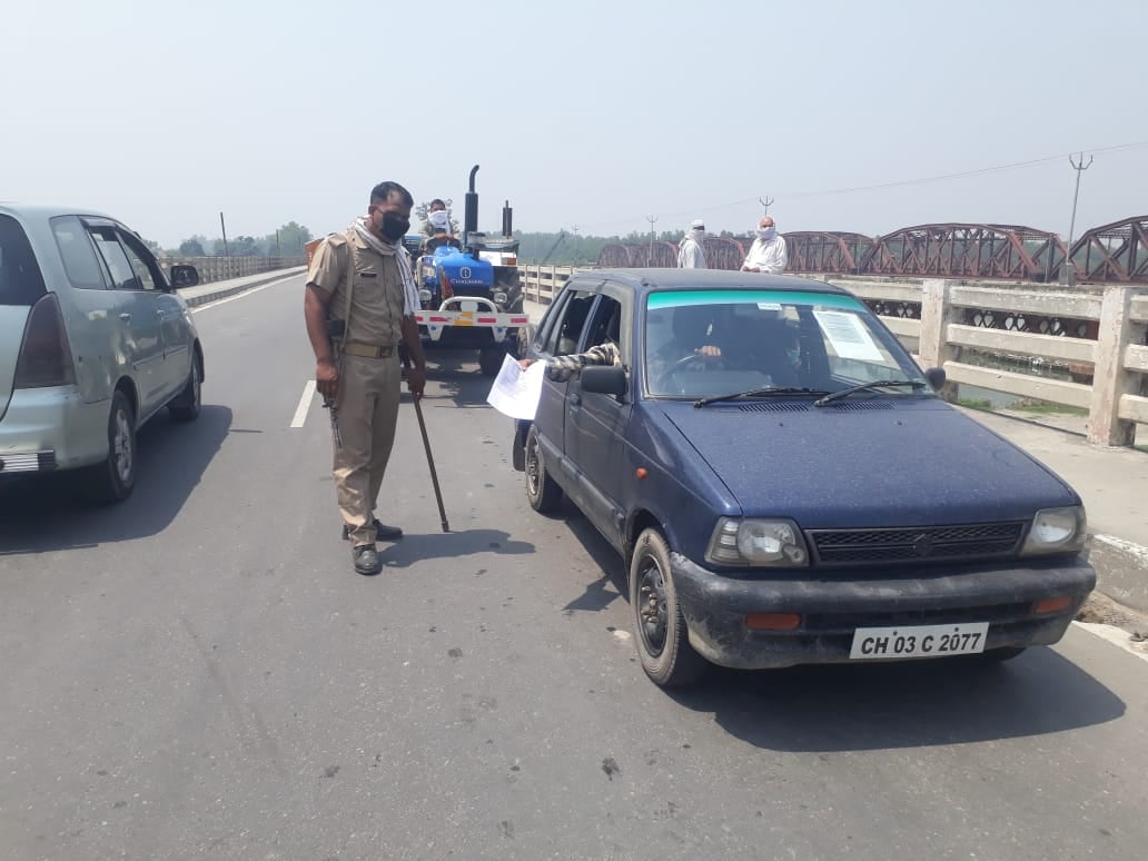कार सवार को रोक कर उसका पास देखता पुलिसकर्मी
