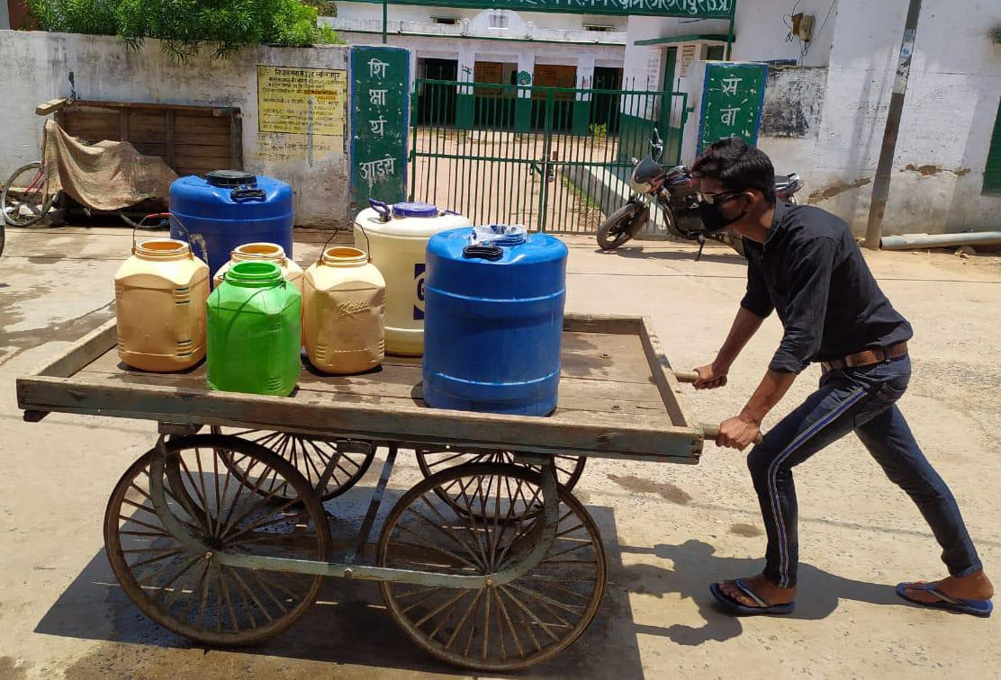 हाथ ठेले पर पानी के बर्तन रखकर पानी ढोता युवक हाथ ठेले पर पानी के बर्तन रखकर पानी ढोता युवक