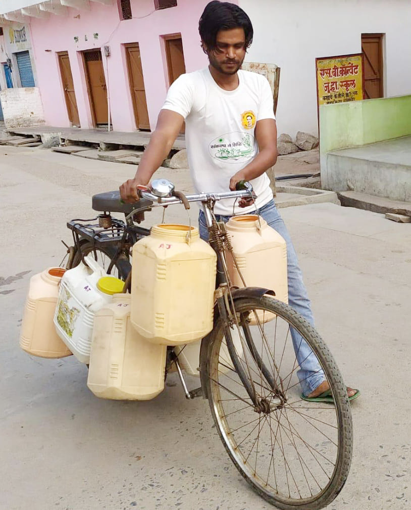 साइकिल पर पानी के डिब्बे टांग कर पानी ढोता युवक