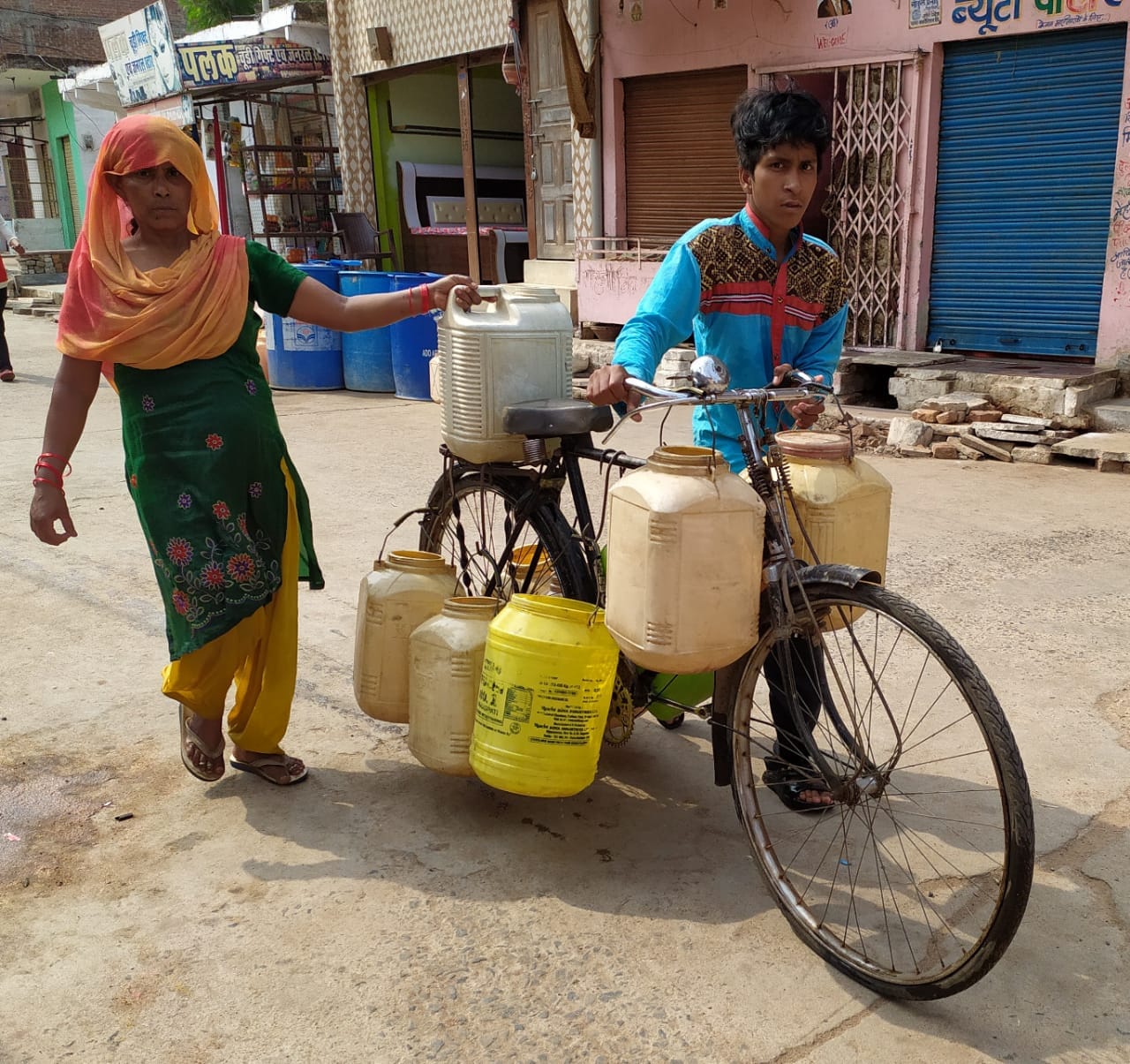 साइकिल पर कुप्पा टांग कर पानी ढोता युवक व महिला साइकिल पर कुप्पा टांग कर पानी ढोता युवक व महिला