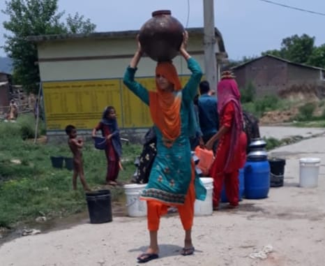 बेहट के खुवाशपुर में हैडपंप से घड़े में पानी भरकर ले जाती महिला।