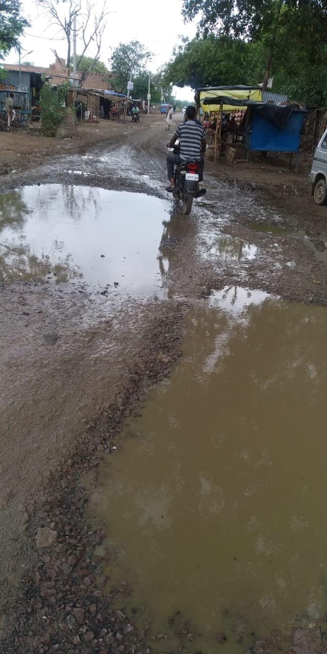 जलभराव से गड्ढे से गुजरती बाइक सवार जलभराव से गड्ढे से गुजरती बाइक सवार