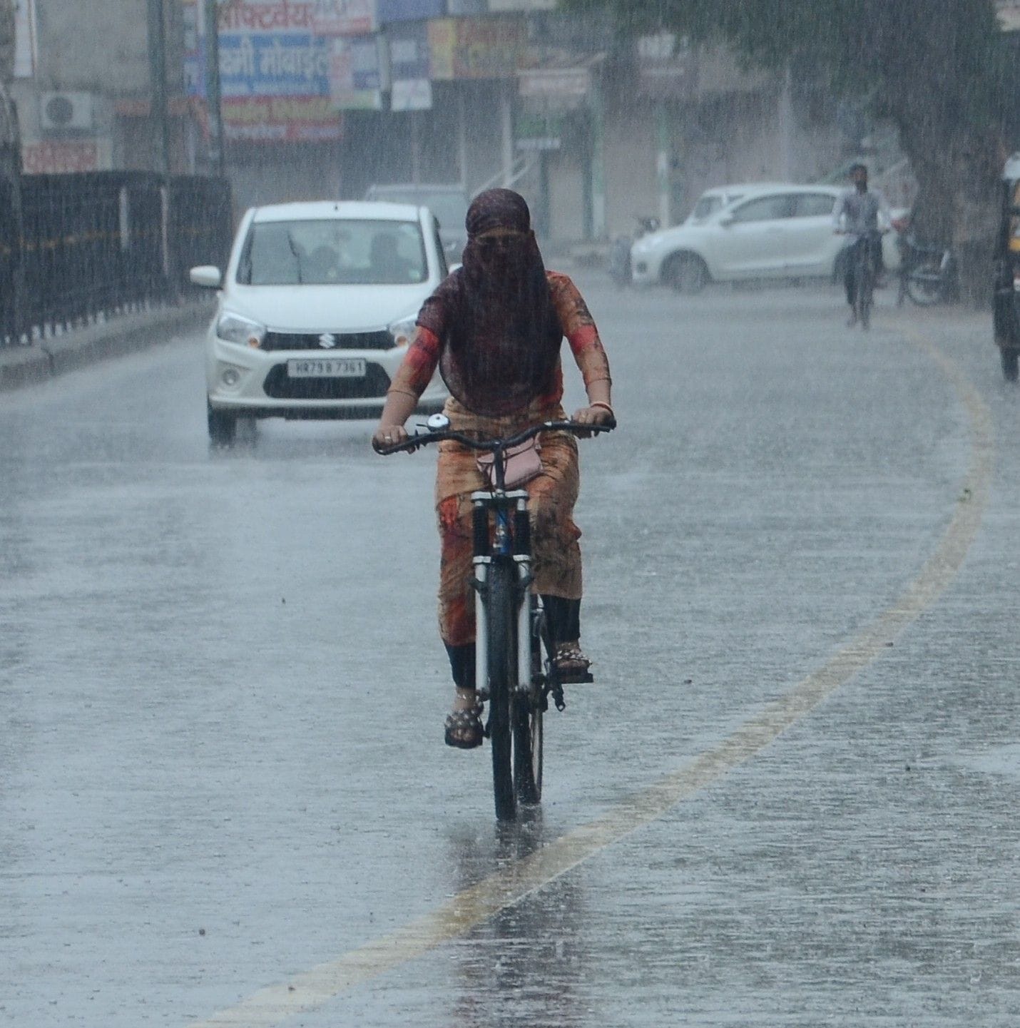 रविवार सुबह बारिश में अपने गंतव्य को जाती साइकिल सवार युवती।