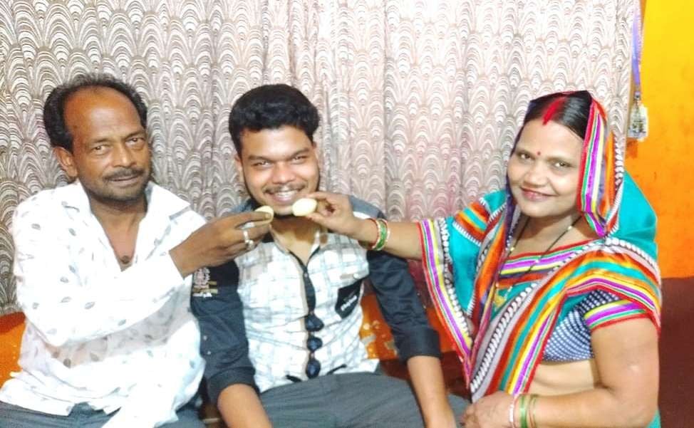 सीबीएसई बोर्ड परीक्षा में अव्वल आने पर अपने पुत्र को मिठाई खिलाते माता-पिता।