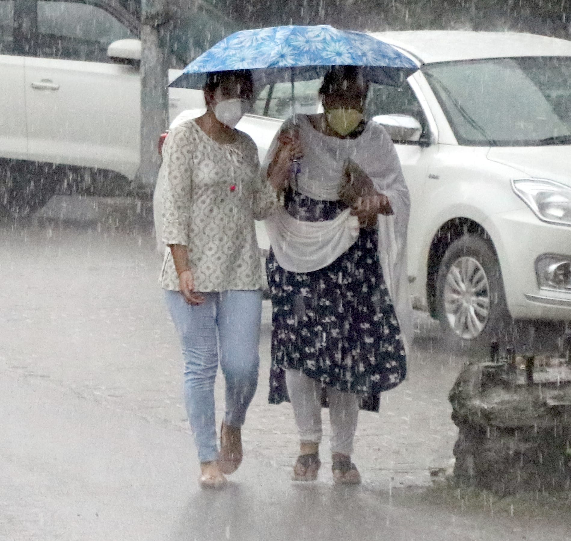 बिजनौर में तेज बारिश में छाता लगाकर जाती युवती और महिला।