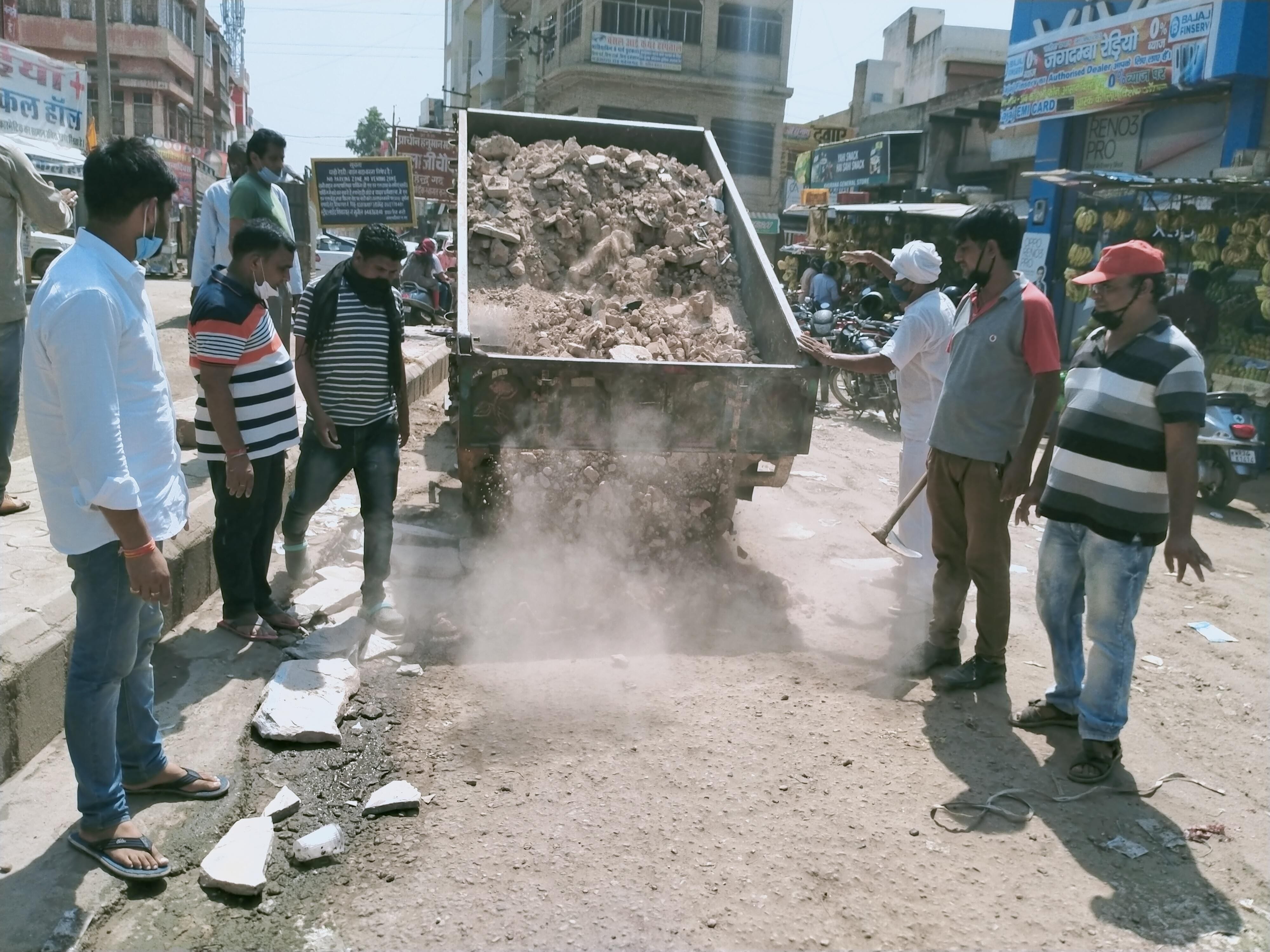 शहर के बालाजी चौक पर सड़क के गड्ढों को भरवाने के लिए रोड़े डलवाते शहरवासी। शहर के बालाजी चौक पर सड़क के गड्ढों को भरवाने के लिए रोड़े डलवाते शहरवासी।