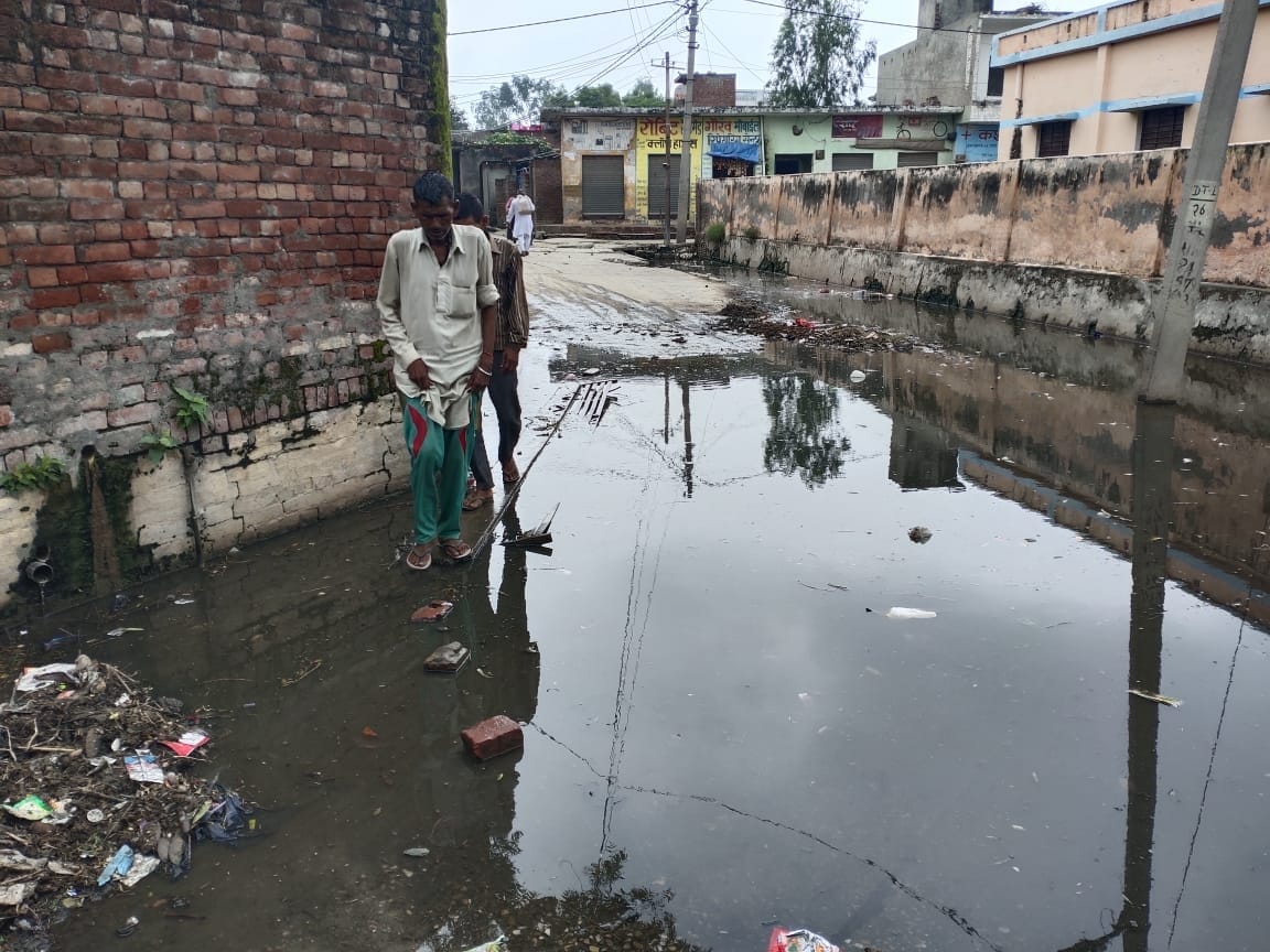 बाबरी में सड़क पर फैले तालाब के गंदे पानी से होकर गुजरते लोग।