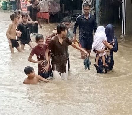 झिंझाना में बरसात के बाद सडक पर  पानी भरने के बाद मस्ती व बच्चे को लेकर गुजरती महिला