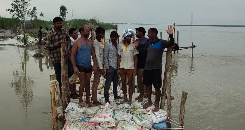 मिट्टी से भरे बोरे तथा बल्लियां लगाकर  तटबंध को ठीक करने में जुटे मजदूर।