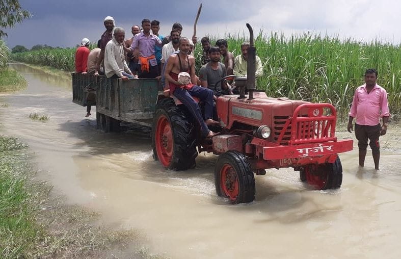 रास्ते में भरे पानी में ट्रैक्टर पर सवार होकर गुजरते लोग।