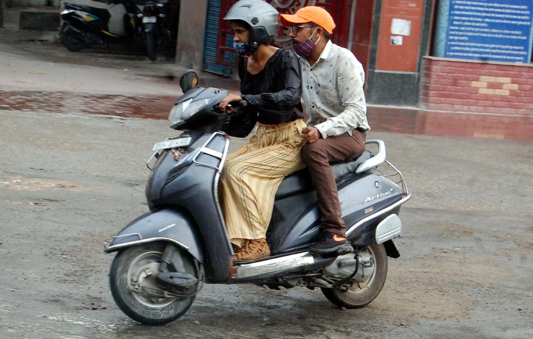 बारिश के दौरान दुपहिए से जाते राहगीर।