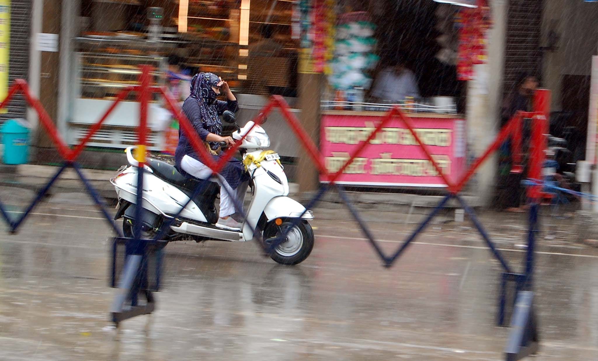 शहर में बारिश के दौरान स्कूटी से जाती युवती।