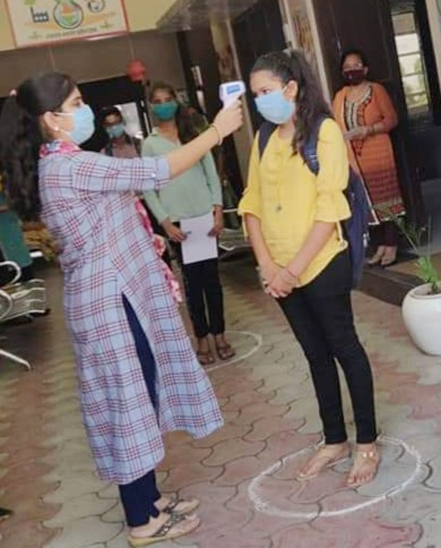 स्कूल के गेट पर छात्रा की थर्मल स्क्रीनिंग करती अध्यापिका। स्कूल के गेट पर छात्रा की थर्मल स्क्रीनिंग करती अध्यापिका।