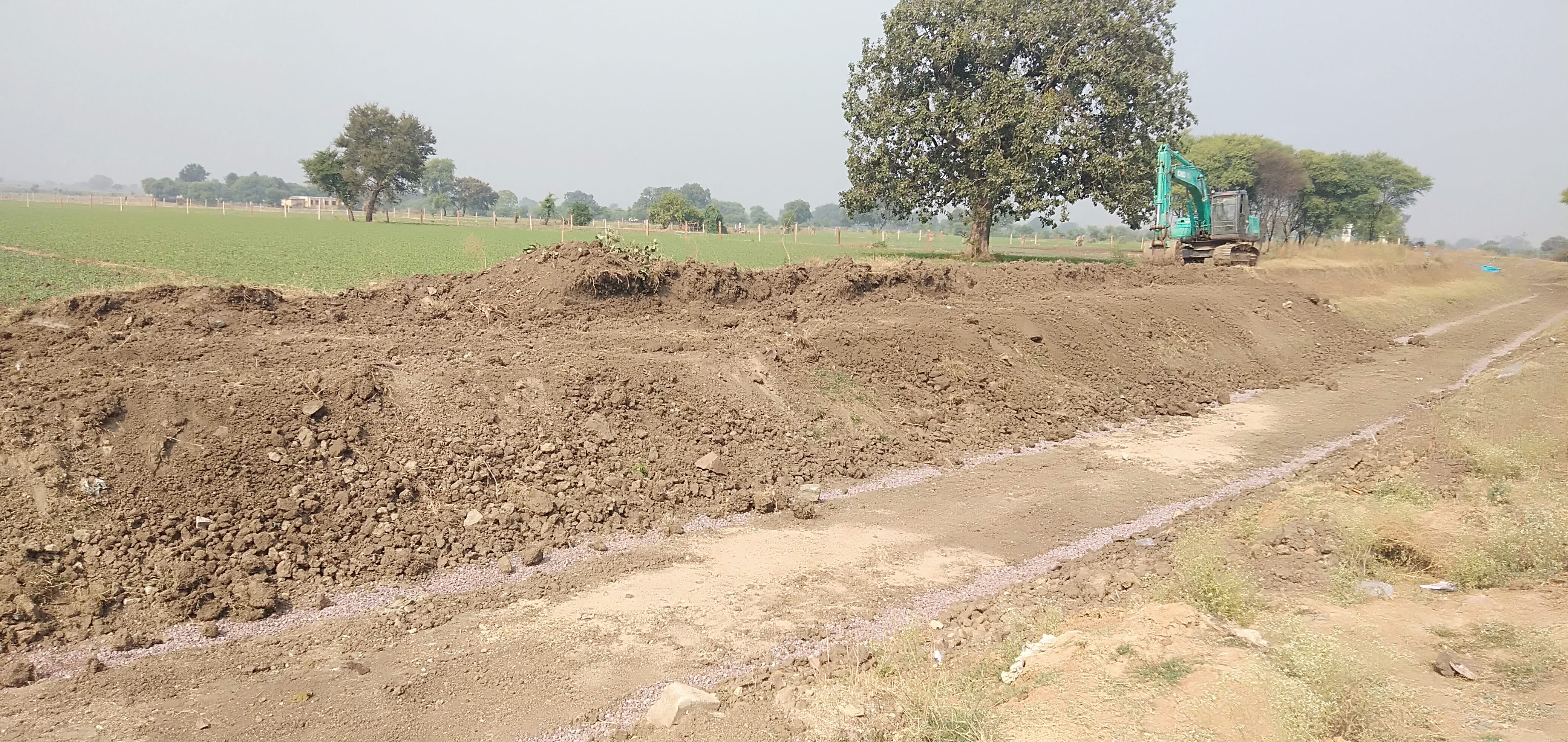 नहर में काम करती एल एन टी और नहर के पास खड़ी फसल सिचाई के इंतजार में नहर में काम करती एल एन टी और नहर के पास खड़ी फसल सिचाई के इंतजार में