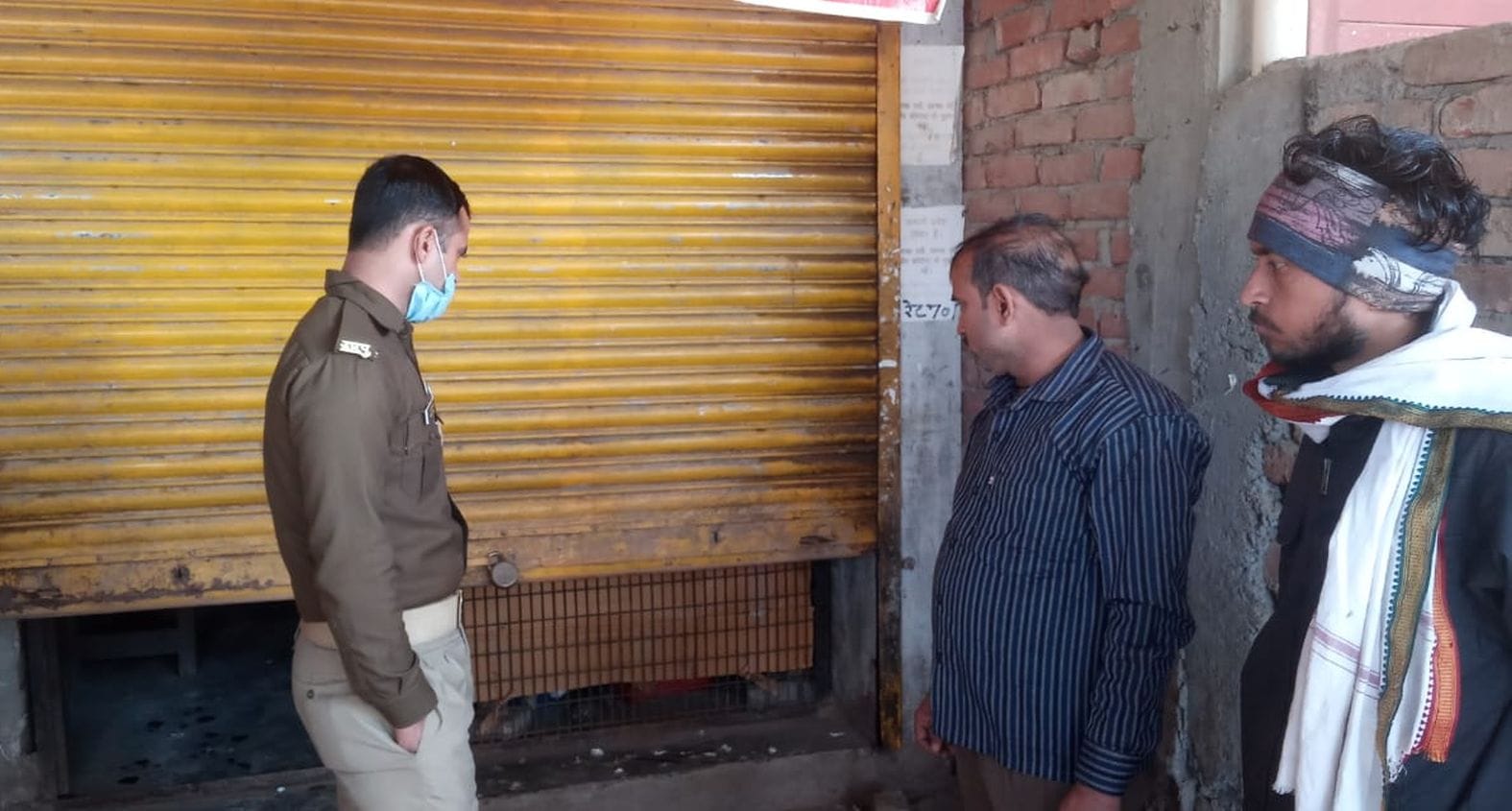 शराब की दुकान में चोरी के बाद टूटे शटर को देखता पुलिस कर्मी व अन्य । संवाद शराब की दुकान में चोरी के बाद टूटे शटर को देखता पुलिस कर्मी व अन्य । संवाद