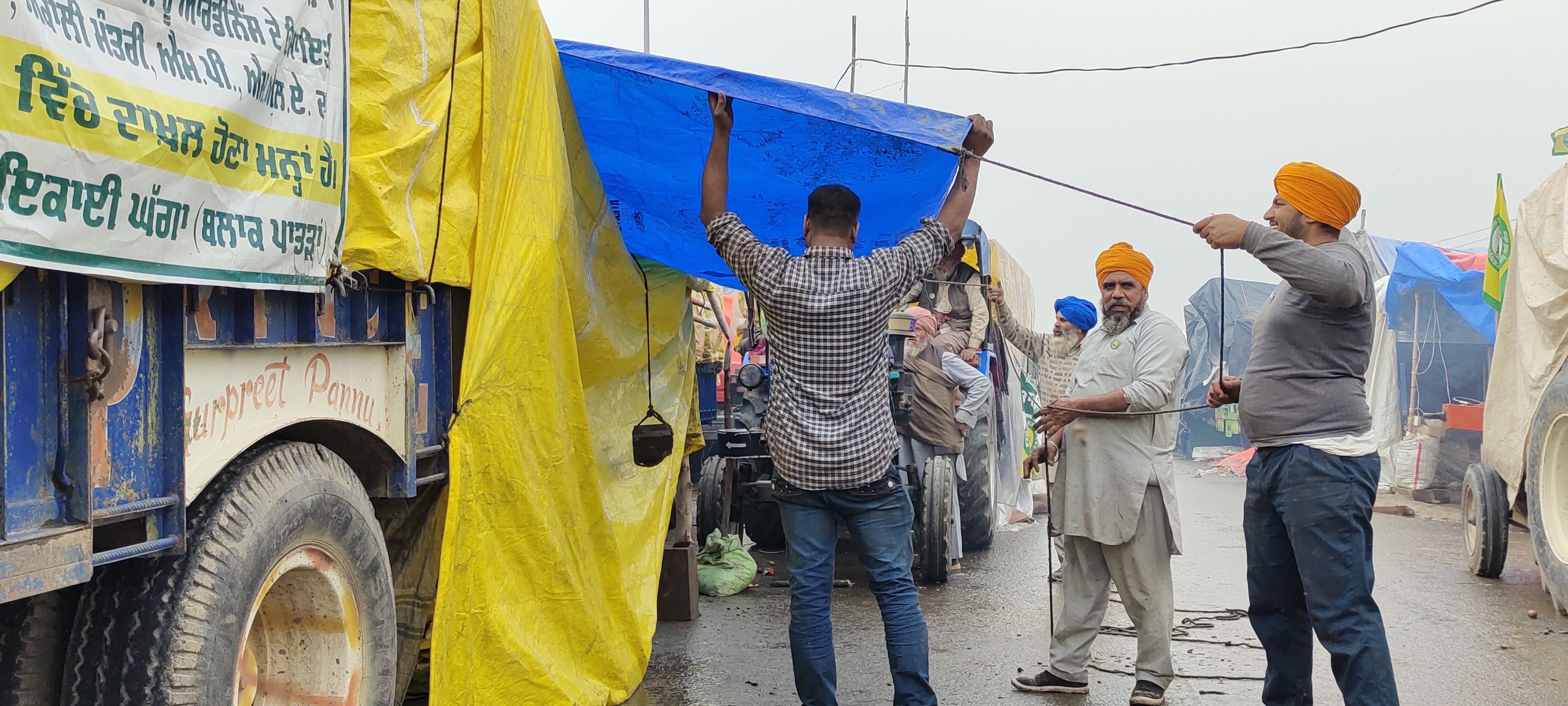ट्रॉली में लगाए गए अपने तंबू को बारिश से बचाने का इंतजाम करते किसान। संवाद ट्रॉली में लगाए गए अपने तंबू को बारिश से बचाने का इंतजाम करते किसान। संवाद