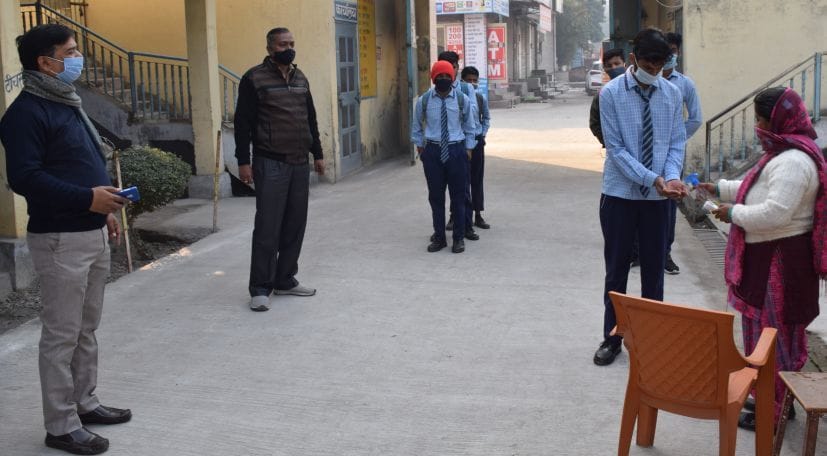 रुद्रपुर के जनता इंटर कॉलेज में बच्चों को सैनिटाइजर लगाती कर्मचारी।