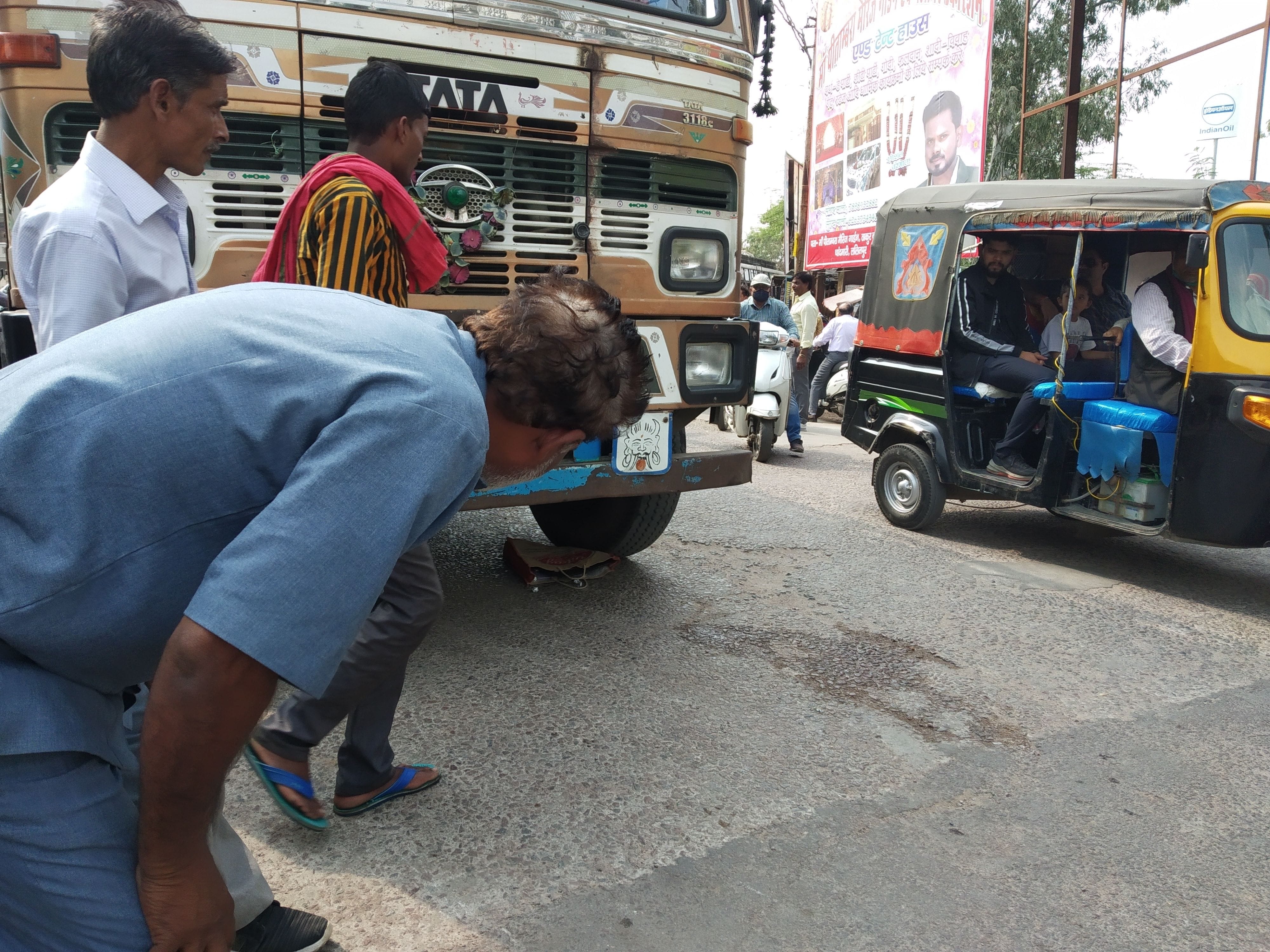 ट्रक के नीचे दबा बैग देखता व्यक्ति