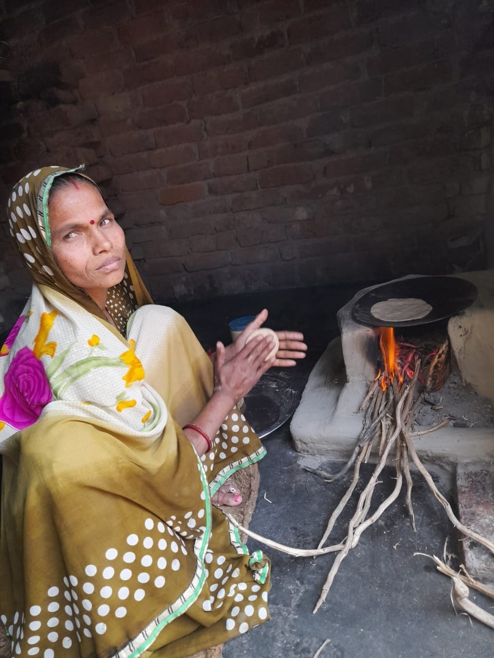 खैर के गांव मानपुर स्थित अपने घर पर चूल्हे पर खाना पकाती महिला।