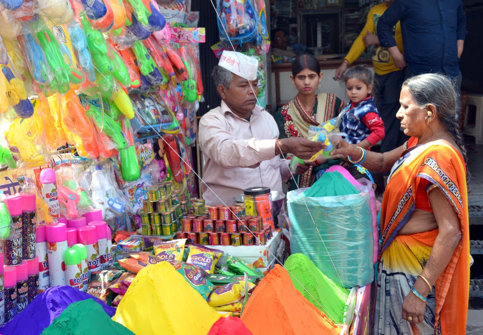 बच्चों के लिए बाजार में पिचकारी खरीदती महिला। संवाद बच्चों के लिए बाजार में पिचकारी खरीदती महिला। संवाद