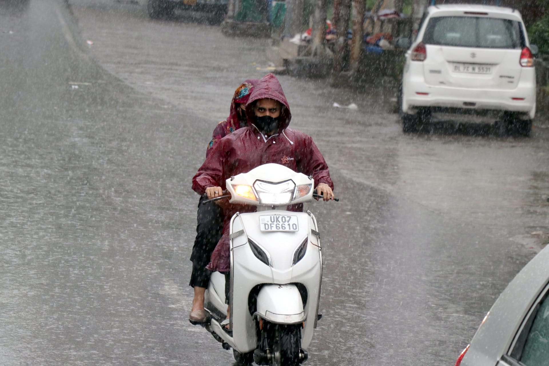 बिजनौर में बारिश में भीगते स्कूटी सवार।