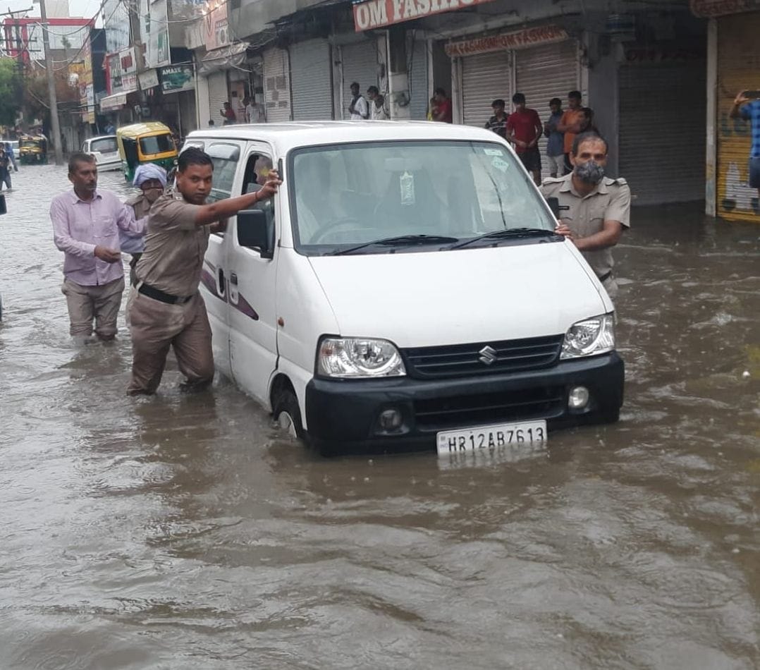 ककरोई चौक पर दो फुट भरे पानी के बीच बंद ईको वैन को धक्का मारकर ले जाते पुलिस कर्मी। संवाद