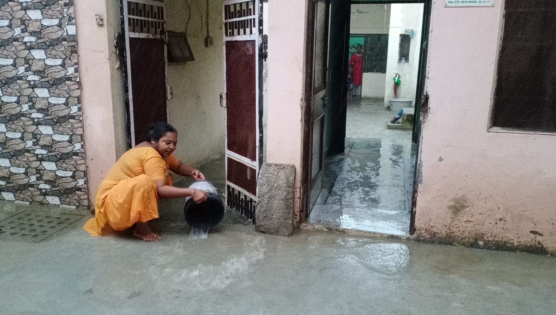 घर में घुसा बारिश का पानी निकालती महिला। संवाद घर में घुसा बारिश का पानी निकालती महिला। संवाद
