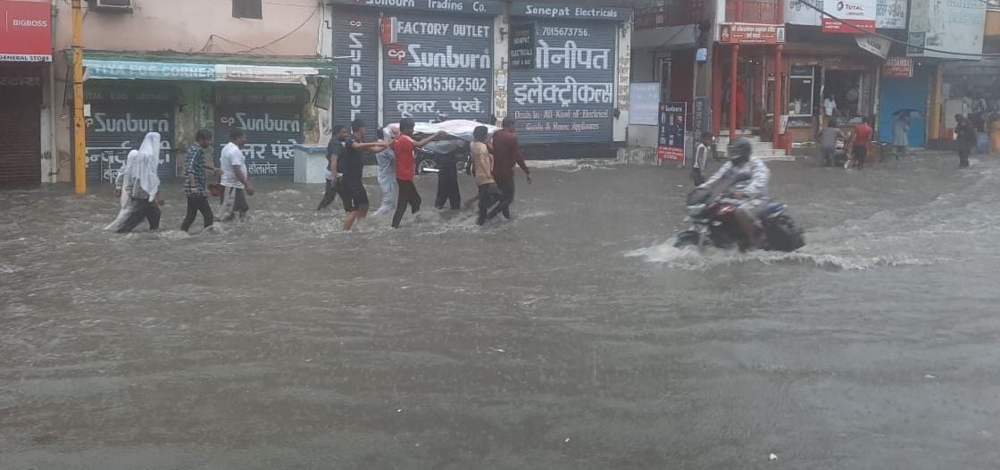 गोहाना रोड पर भरे पानी में बारिश के दौरान दाह संस्कार के लिए शव को लेकर जाते परिजन। संवाद गोहाना रोड पर भरे पानी में बारिश के दौरान दाह संस्कार के लिए शव को लेकर जाते परिजन। संवाद