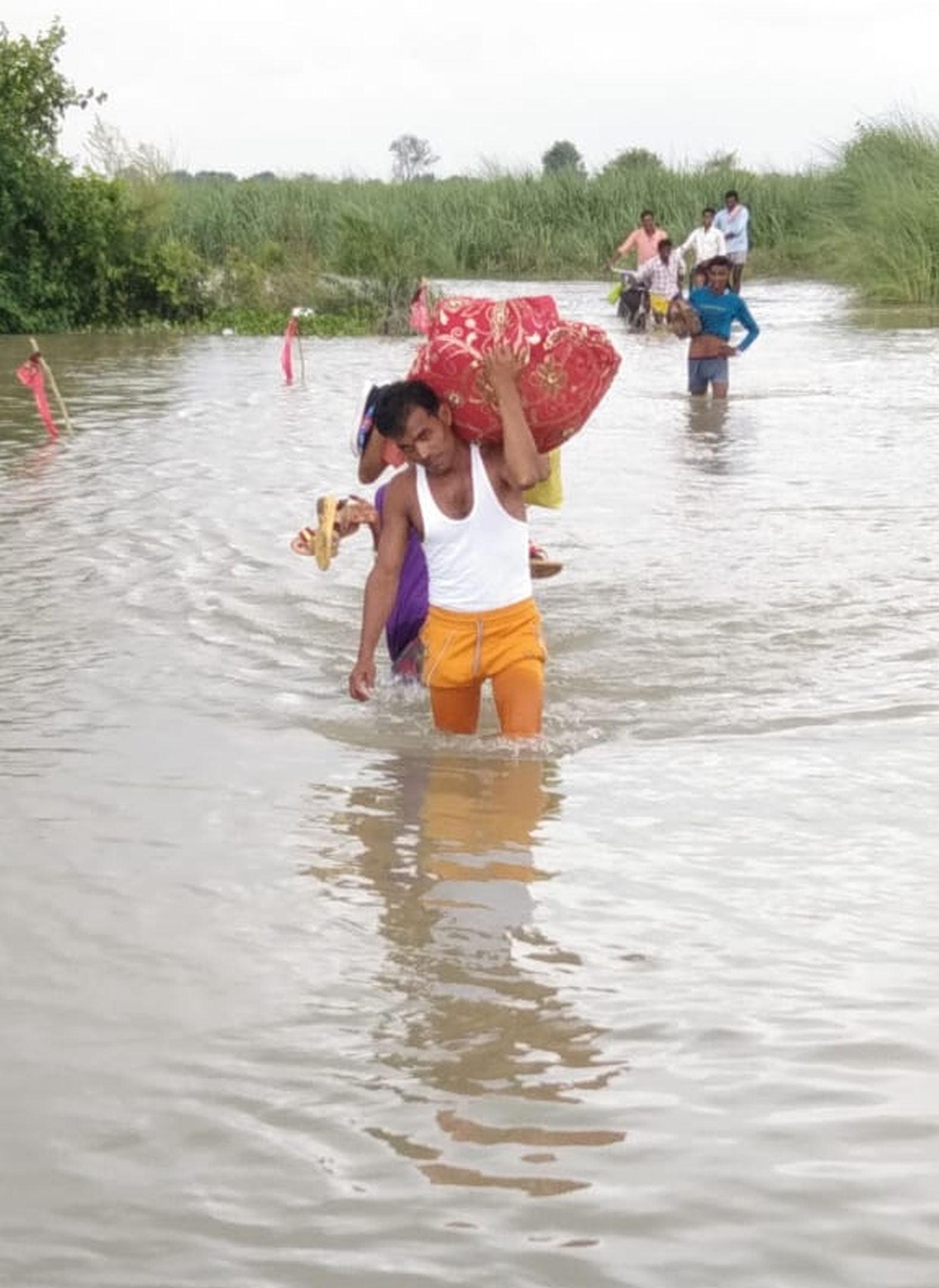 गांव पंखियन की मड़ैया से दूल्हे के सेहरे को ढलिया में रखाकर बाढ़ के पानी से गुजरते परिजन। संवाद