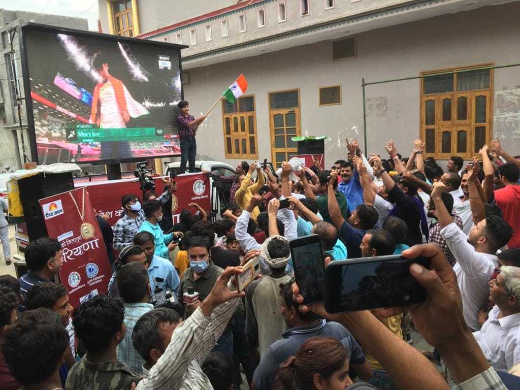 गांव खंडरा में घर के बाहर नीरज को स्क्रीन पर देखते लोग , मोबाइल से फोटो लेते हुए गांव खंडरा में घर के बाहर नीरज को स्क्रीन पर देखते लोग , मोबाइल से फोटो लेते हुए