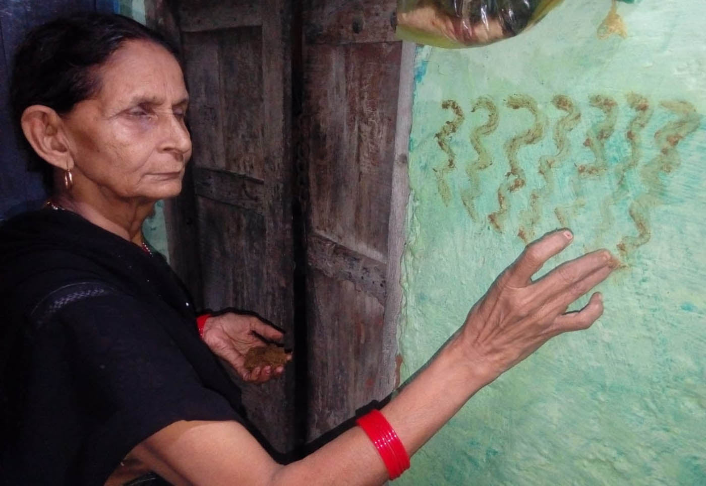 रमेड़ी मोहल्ले में घर के दरवाजे पर गाय के गोवर से नाग आकृति बनाती महिला। रमेड़ी मोहल्ले में घर के दरवाजे पर गाय के गोवर से नाग आकृति बनाती महिला।