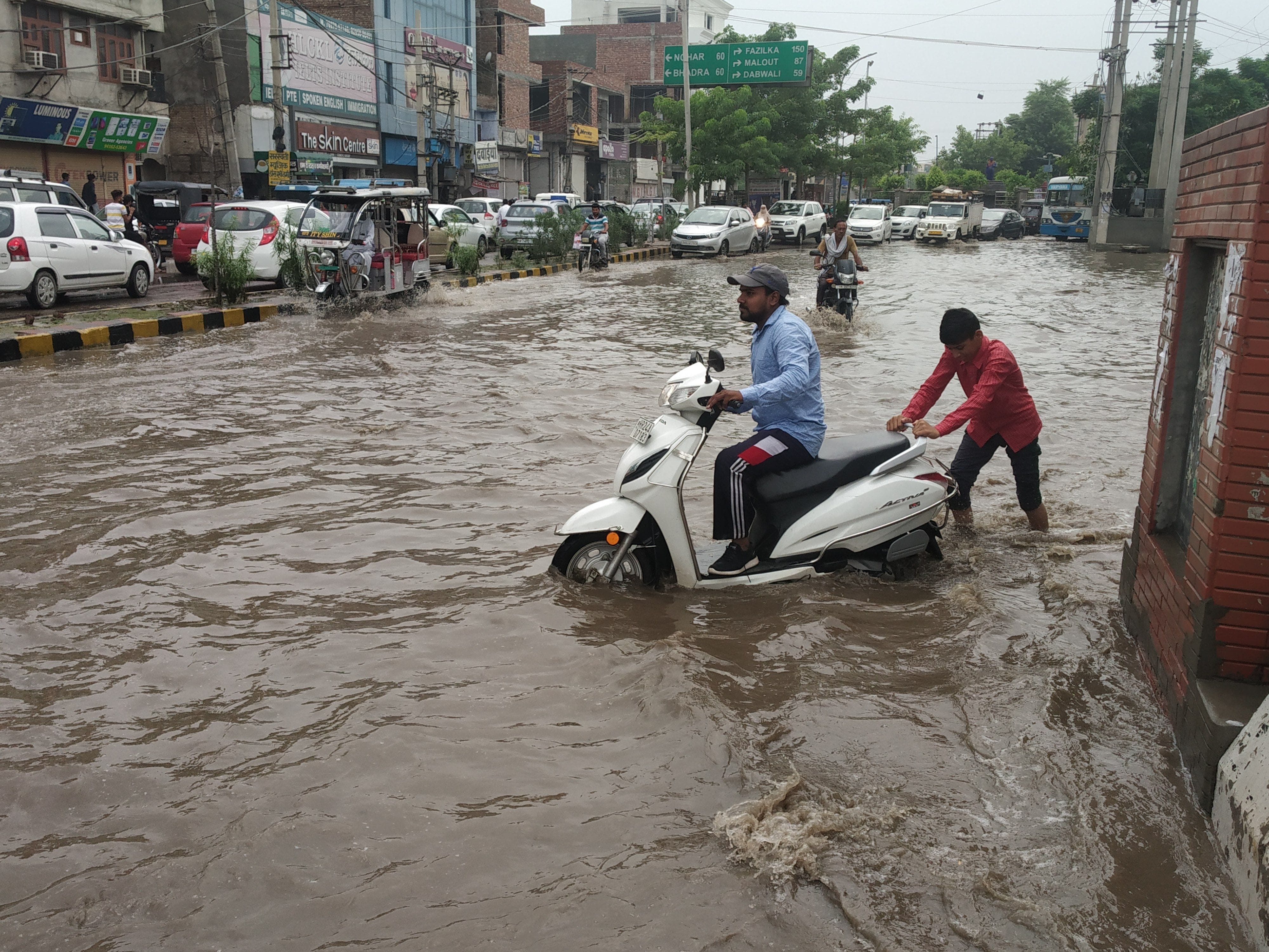 सुरखाब चौक पर जलभराव के कारण बंद हुई स्कूटी को धक्का लगाता युवक 