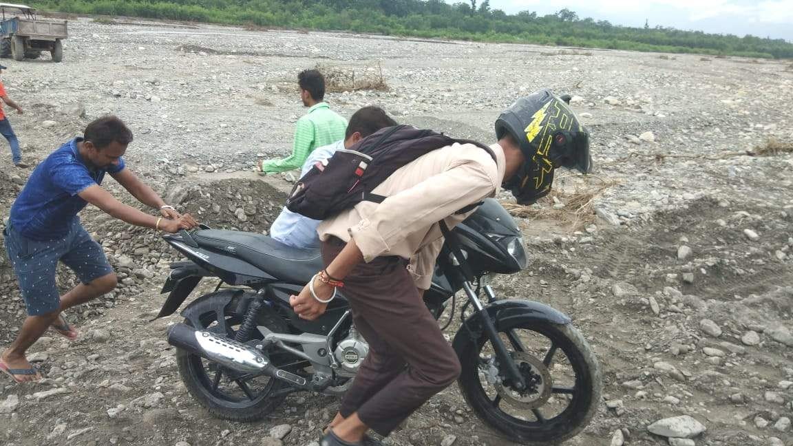  घंमडपुर में जाखन नदी पार बाइक को धक्का देकर लाते युवा।