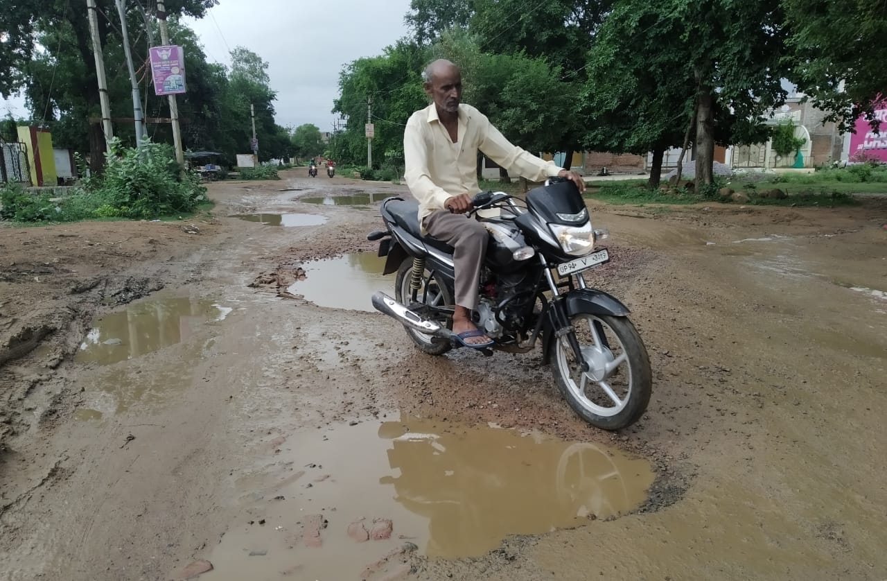 गड्ढों के बीच से निकलता बाइक सवार गड्ढों के बीच से निकलता बाइक सवार