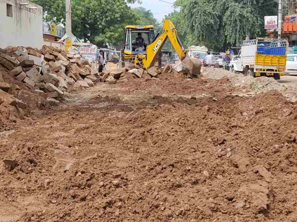 शहर थाना के पास टूटी सड़क को ठीक करती जेसीबी । संवाद
