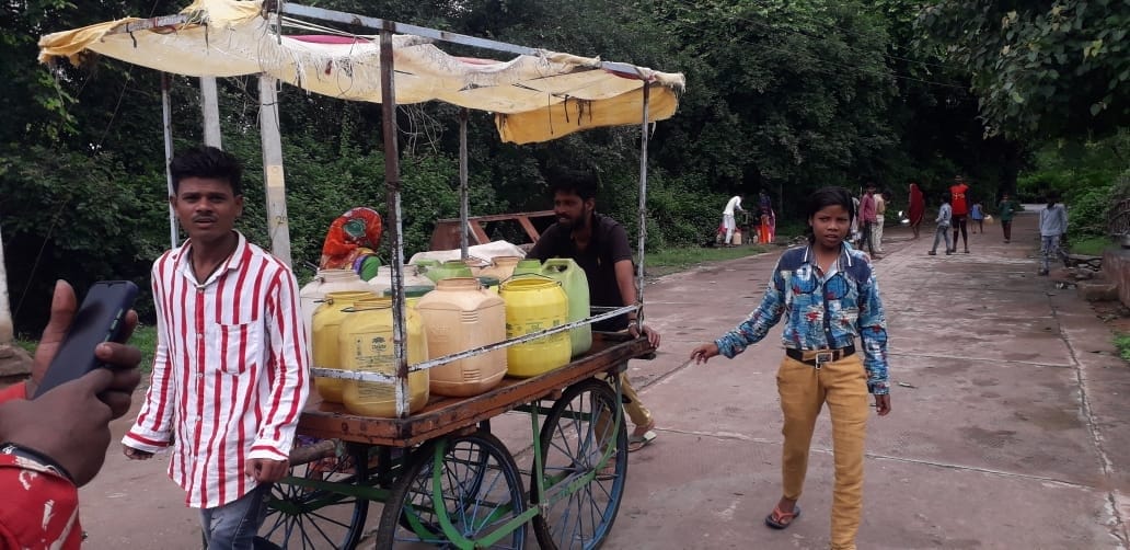 हाथ ठेले पर रखकर पानी के डिव्बे ले जाता व्यक्ति हाथ ठेले पर रखकर पानी के डिव्बे ले जाता व्यक्ति