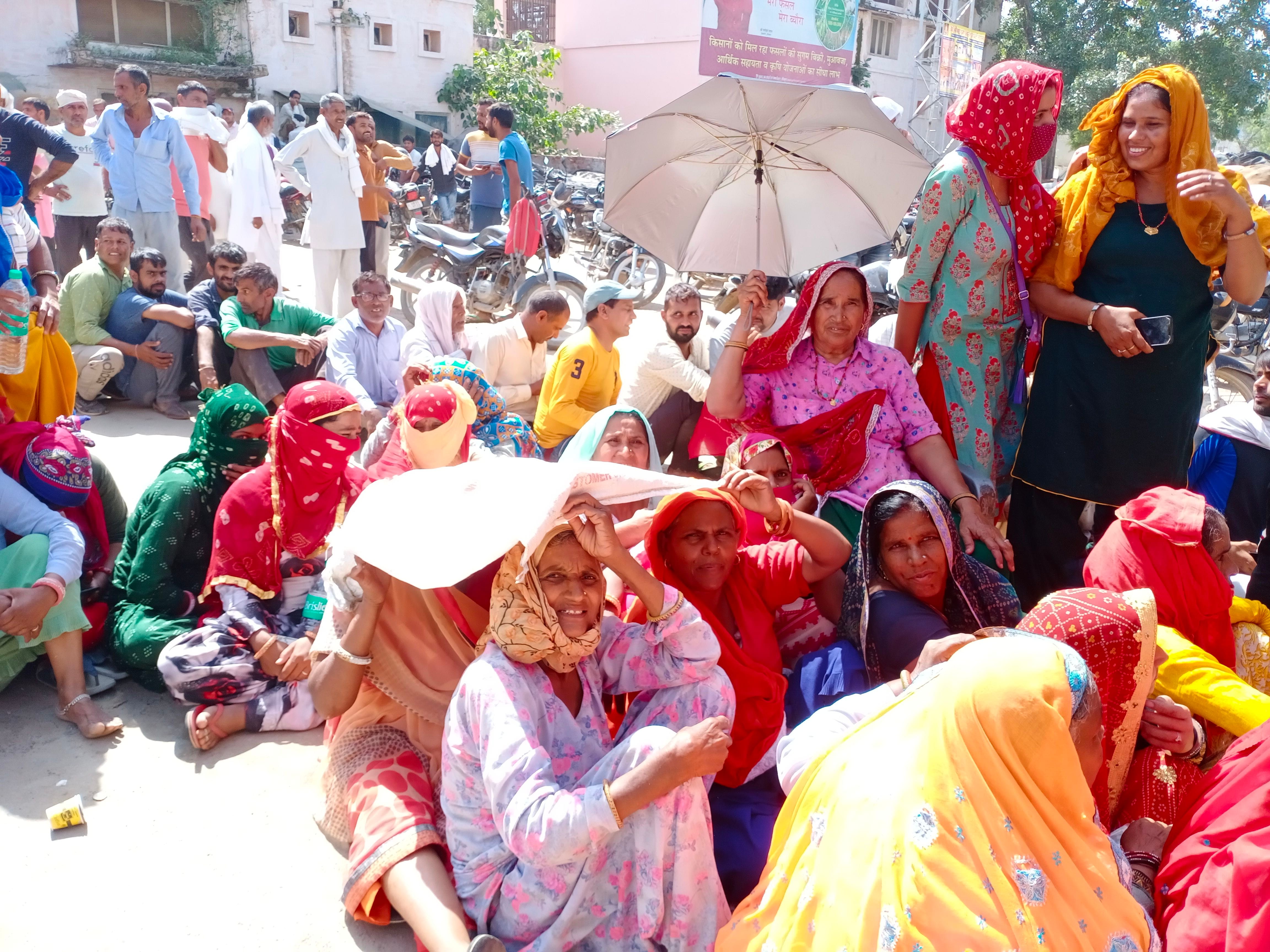 खाद लेने के लिए लाईन में धूप से बचने के लिए छता लेकर बैठी महिला । खाद लेने के लिए लाईन में धूप से बचने के लिए छता लेकर बैठी महिला ।