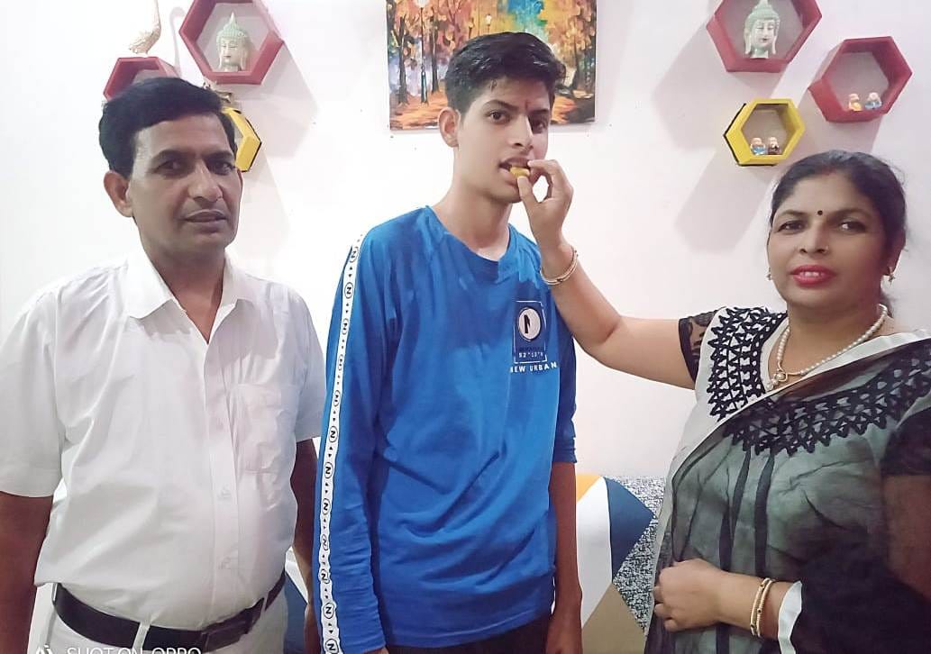 उज्जवल को मिठाई खिलाते माता-पिता। उज्जवल को मिठाई खिलाते माता-पिता।